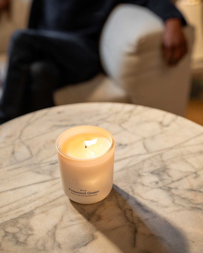 Lit Firewood Green candle on a marble table beside a sofa.