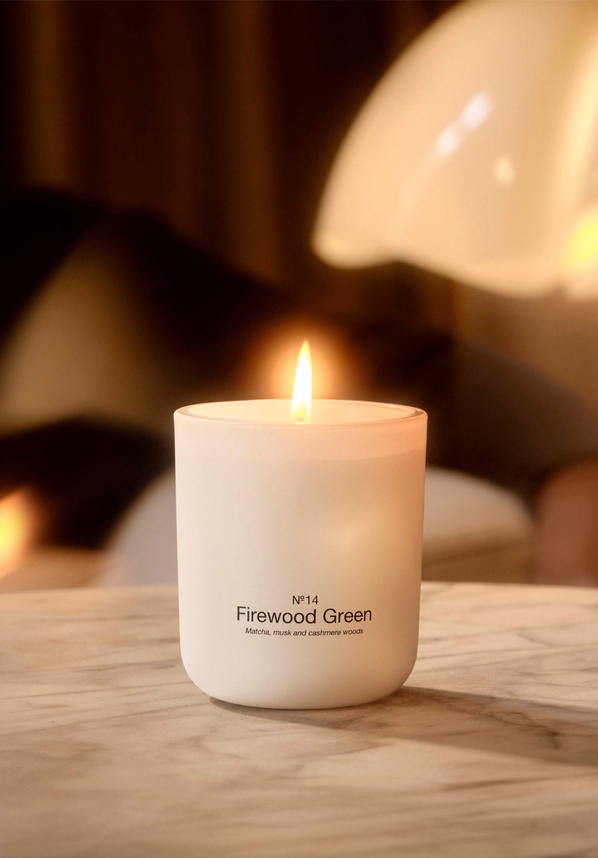 A lit No. 14 Firewood Green scented candle on a marble table in warm light.