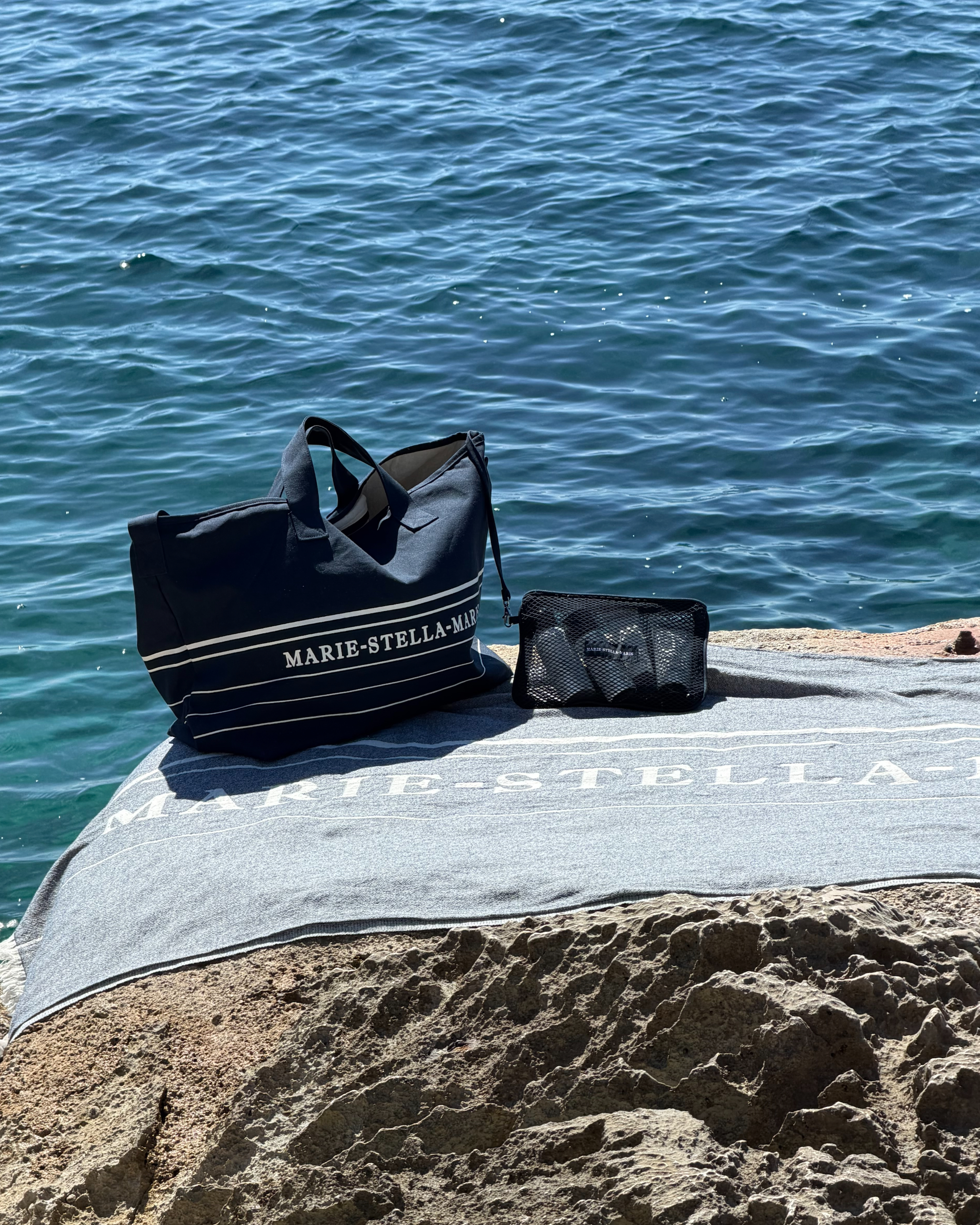 Marie-Stella-Maris beach essentials, including a weekend bag and towel, set beside the turquoise sea at Cala Deià, Mallorca.
