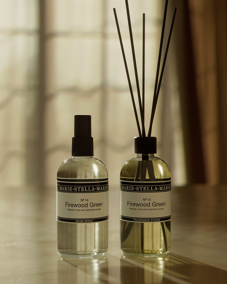 Marie-Stella-Maris No. 14 Firewood Green room spray and fragrance diffuser with black reeds, displayed in warm sunlight against a softly blurred window. The fragrance features notes of matcha, musk and cashmere woods.