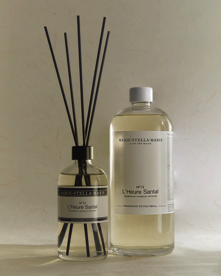Marie-Stella-Maris No.13 L'Heure Santal Fragrance Sticks displayed alongside the 750 ml Fragrance Sticks Refill. The diffuser with black fragrance reeds and the refill bottle are presented together, highlighting the refillable design and the fragrance's warm notes of sandalwood, cardamom and tonka.
