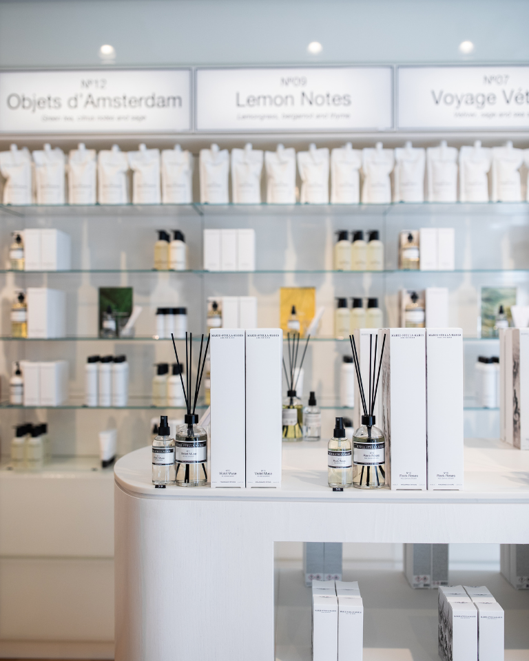 Interior of a Marie-Stella-Maris store featuring a white refill bar with multiple refill bottles, a sink with pump dispensers, and a sign reading ‘REFILL BAR’ above it. A black-and-white ocean photograph hangs on the wall behind the counter, with plants and a branded white balloon adding a clean, modern atmosphere.