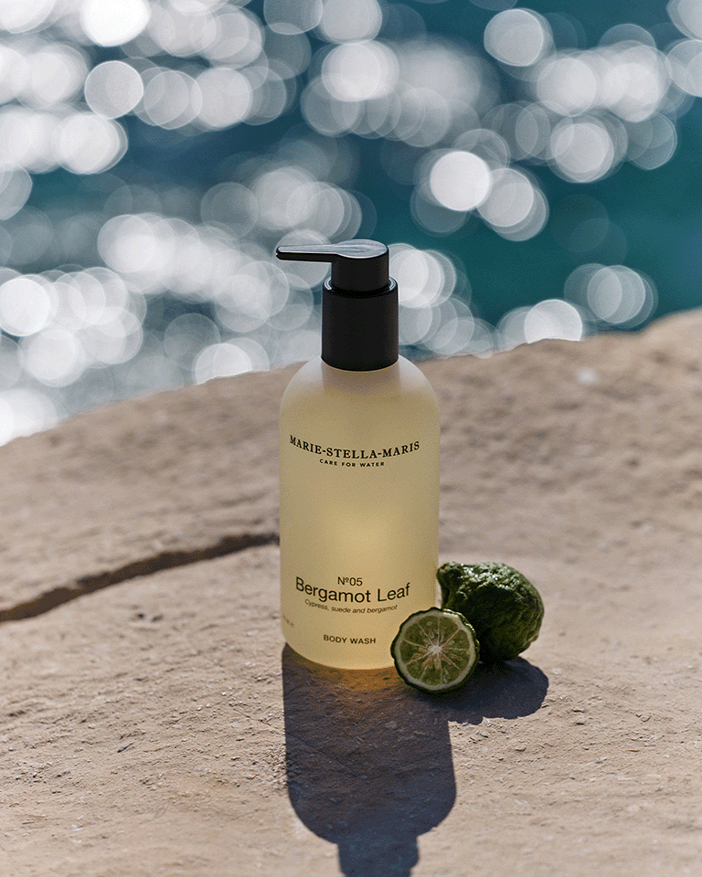 Marie-Stella-Maris No.05 Bergamot Leaf limited edition summer scent body wash 300 ml, displayed on a sunlit stone surface by the sea with fresh bergamot and sparkling water in the background.