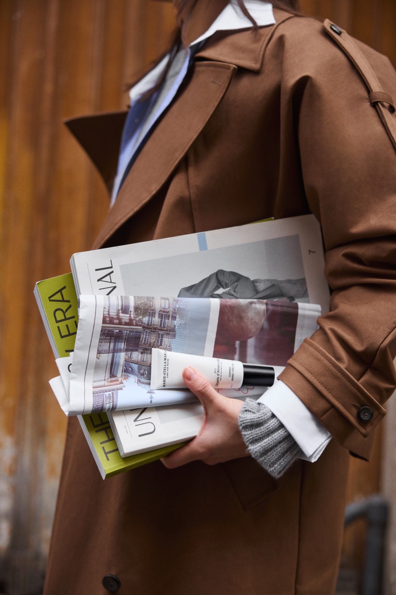 Marie-Stella-Maris Caring Hand Cream No.12 Objets d’Amsterdam 50 ml held in hand with magazines, person wearing a brown coat in the background.