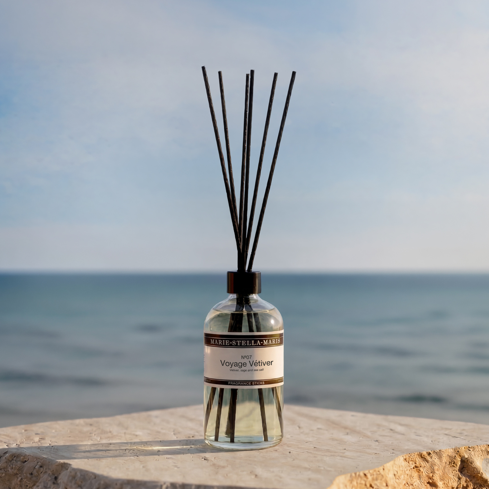 Marie-Stella-Maris No.07 Voyage Vétiver fragrance sticks 250 ml, displayed on a stone surface overlooking the sea, highlighting fragrance notes of vetiver, sage, and sea salt in a calm coastal setting.