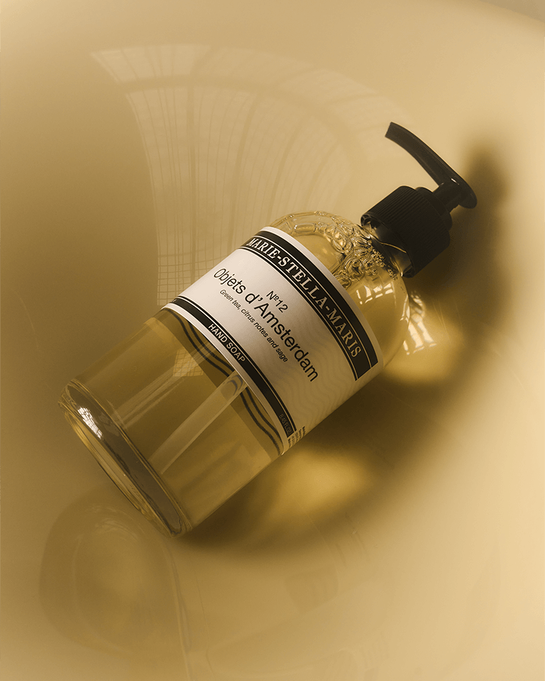 Marie-Stella-Maris No.12 Objets d'Amsterdam hand soap 250 ml in a clear bottle with black pump, lying on its side on a warm-toned surface.