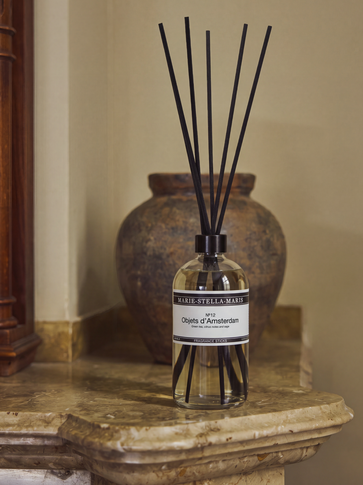 Marie-Stella-Maris home stick scent in No.12 Objets d'Amsterdam sitting on a marble side table in front of a rustic vase on beige khaki background.