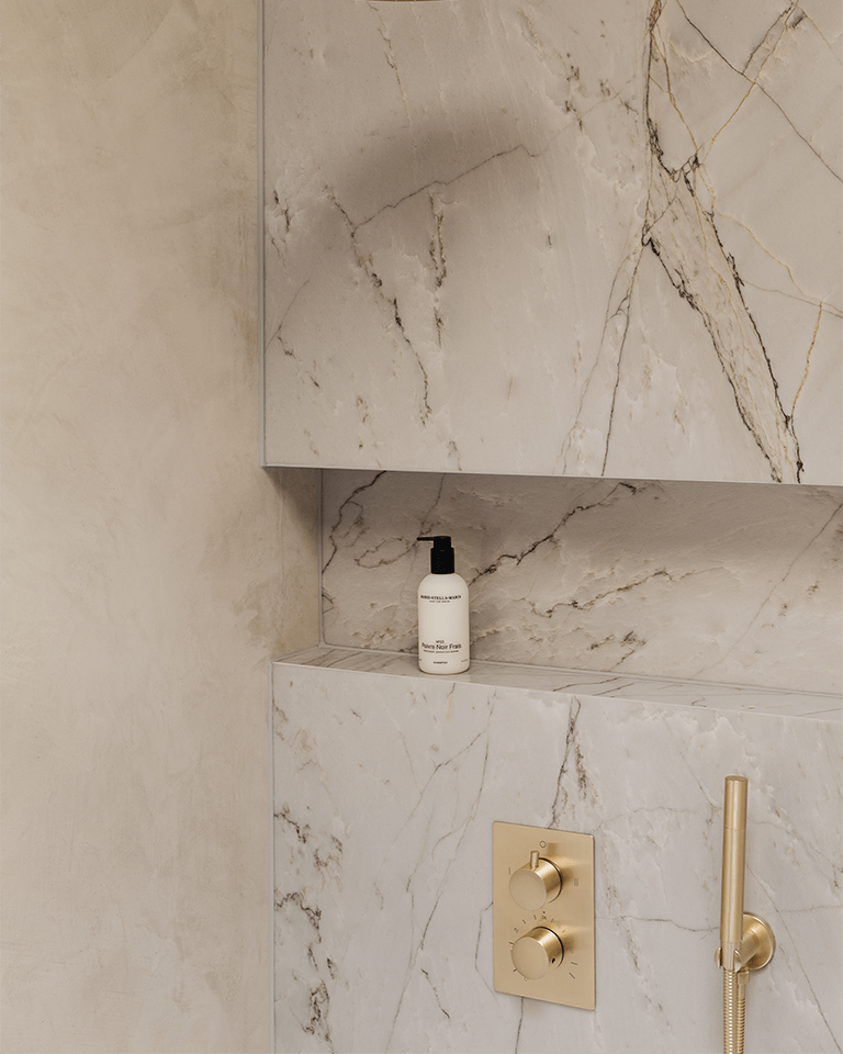 Shampoo Poivre Noir Frais 300 ml bottle on a marble shower shelf with gold faucet controls in a minimalist bathroom.