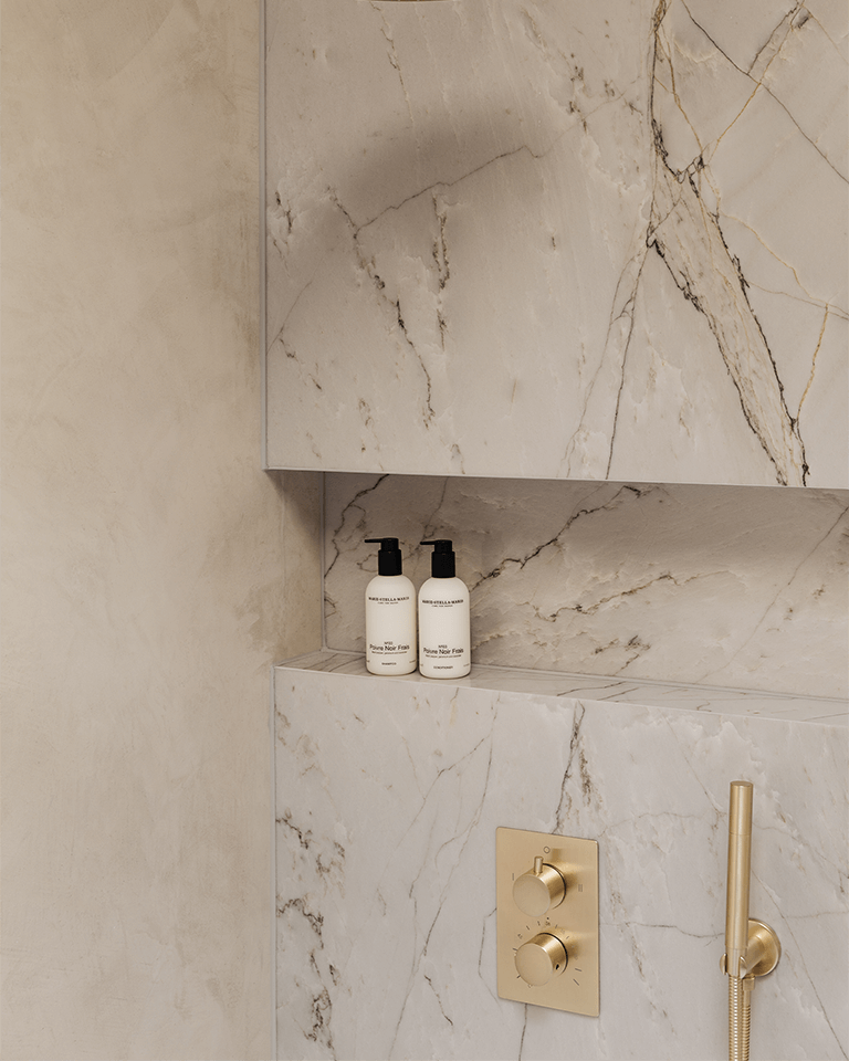 Two white bottles of Shampoo Poivre Noir Frais 300 ml on a beige marble bathroom shelf with gold fixtures