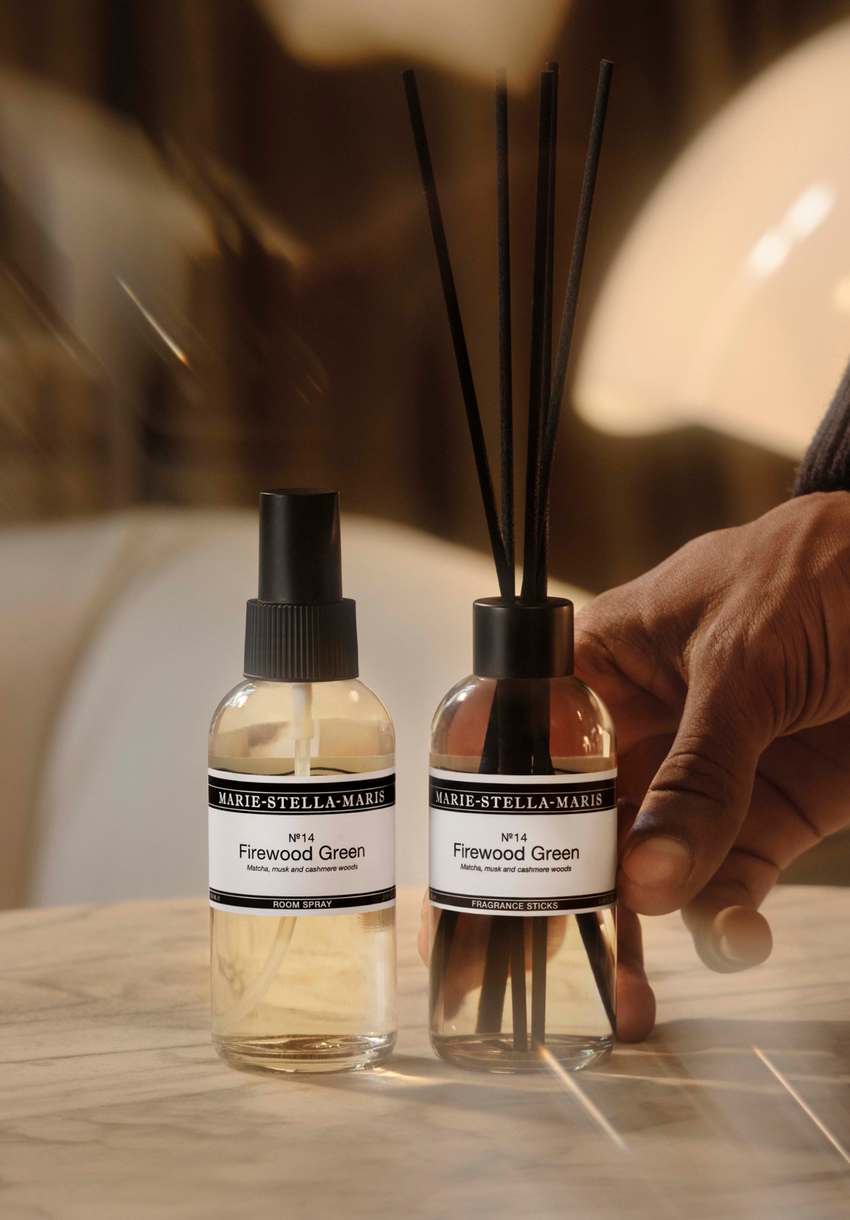 Marie-Stella-Maris No. 14 Firewood Green room spray and fragrance sticks on a marble table, with a hand beside the diffuser.