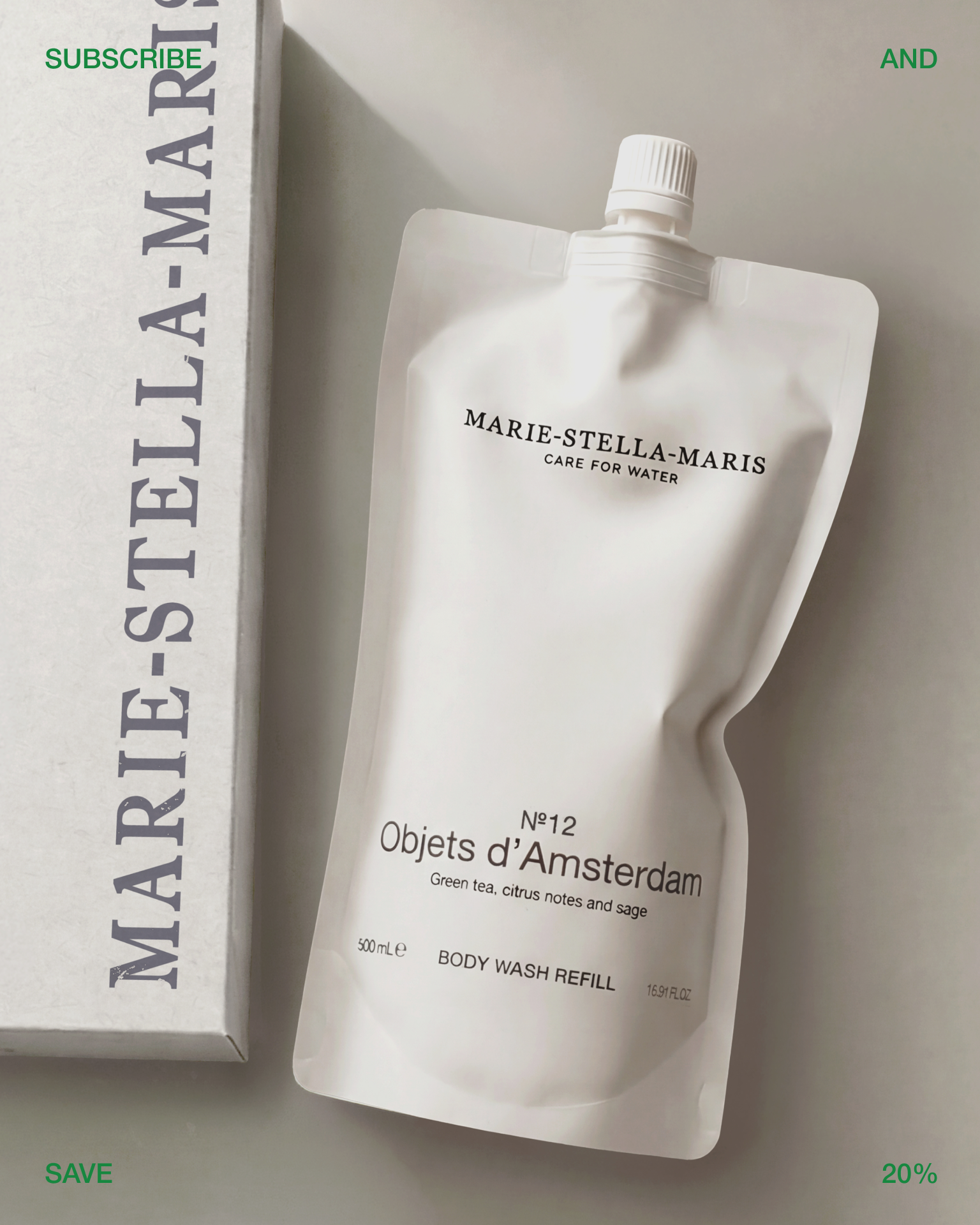 Marie-Stella-Maris No.12 Objets d’Amsterdam body wash refill pouch displayed beside a branded shipping box on a soft neutral background. The refill pouch features the signature scent of green tea, citrus notes, and sage, highlighting the brand’s refillable personal care collection. Green text around the image reads “REFILL,” “AT,” “YOUR,” and “DOORSTEP.”