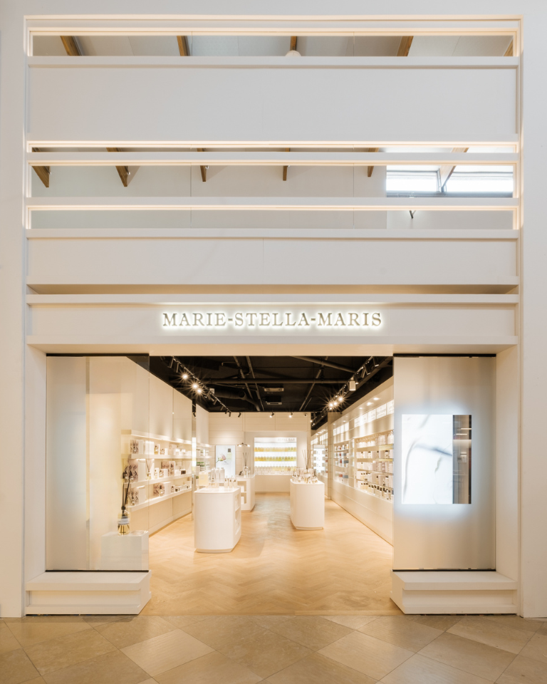 Entrance of a Marie-Stella-Maris store with illuminated sign and a bright, minimalist interior lined with product shelves.