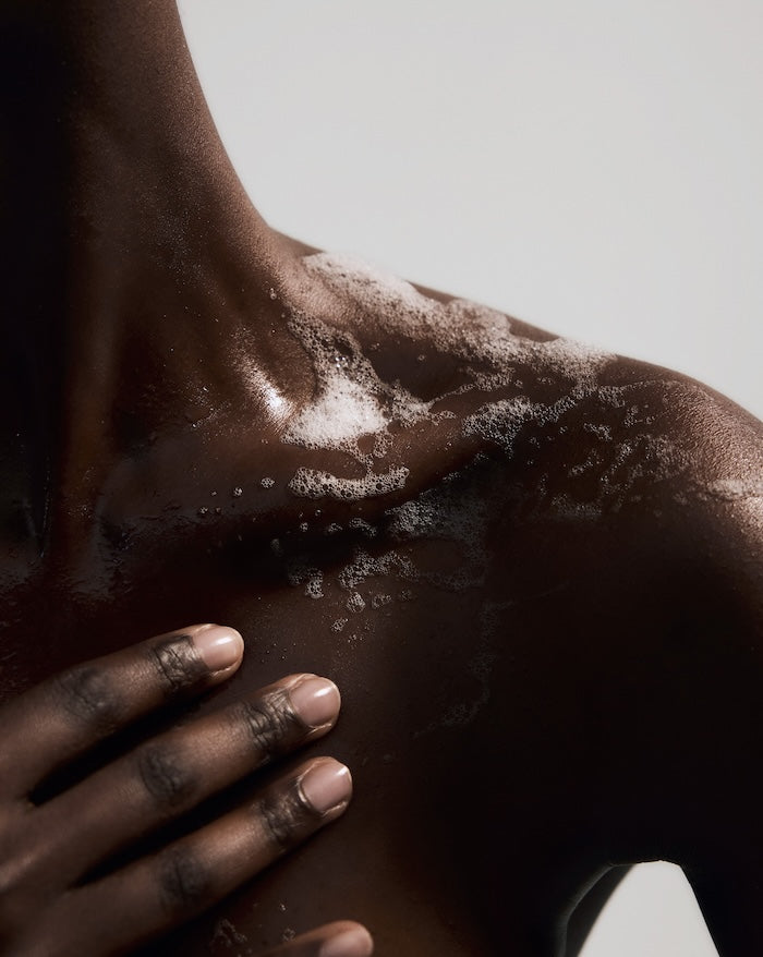 Close-up of dark skin shoulder with foamy lather from natural coconut-based body wash gently applied by hand