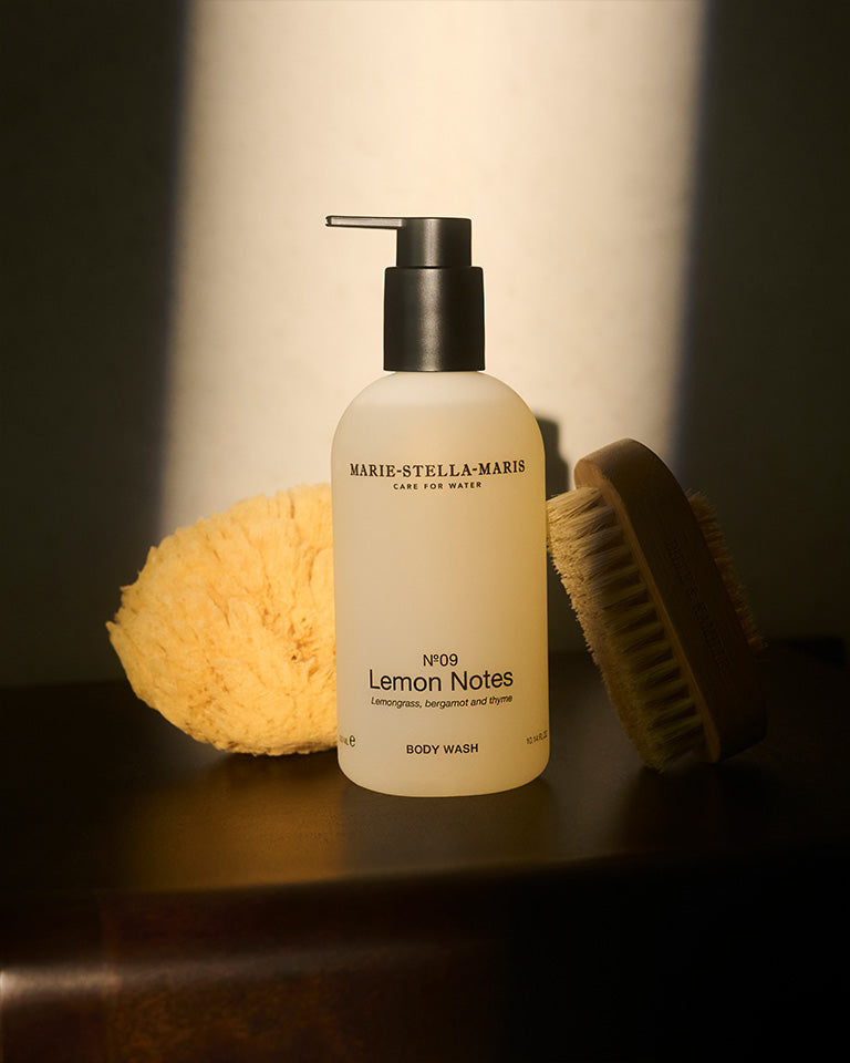 Bottle of Marie-Stella-Maris Lemon Notes body wash 300ml with natural sponge and wooden brush on dark surface