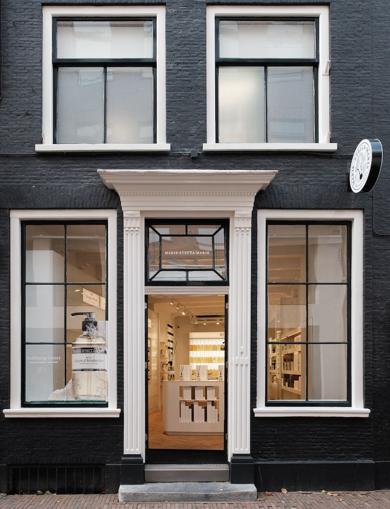 Front of the Marie-Stella-Maris store in Haarlem: black-painted brick facade with white-framed windows and door, looking into a minimalist, well-lit interior.