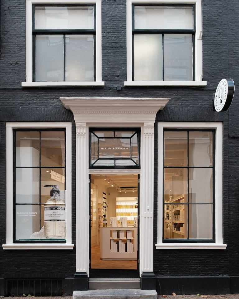 Front of the Marie-Stella-Maris store in Haarlem: black-painted brick facade with white-framed windows and door, looking into a minimalist, well-lit interior.