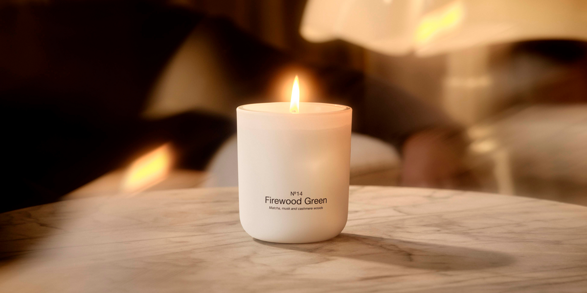 Lit No. 14 Firewood Green candle on a marble table, surrounded by warm, soft light.”