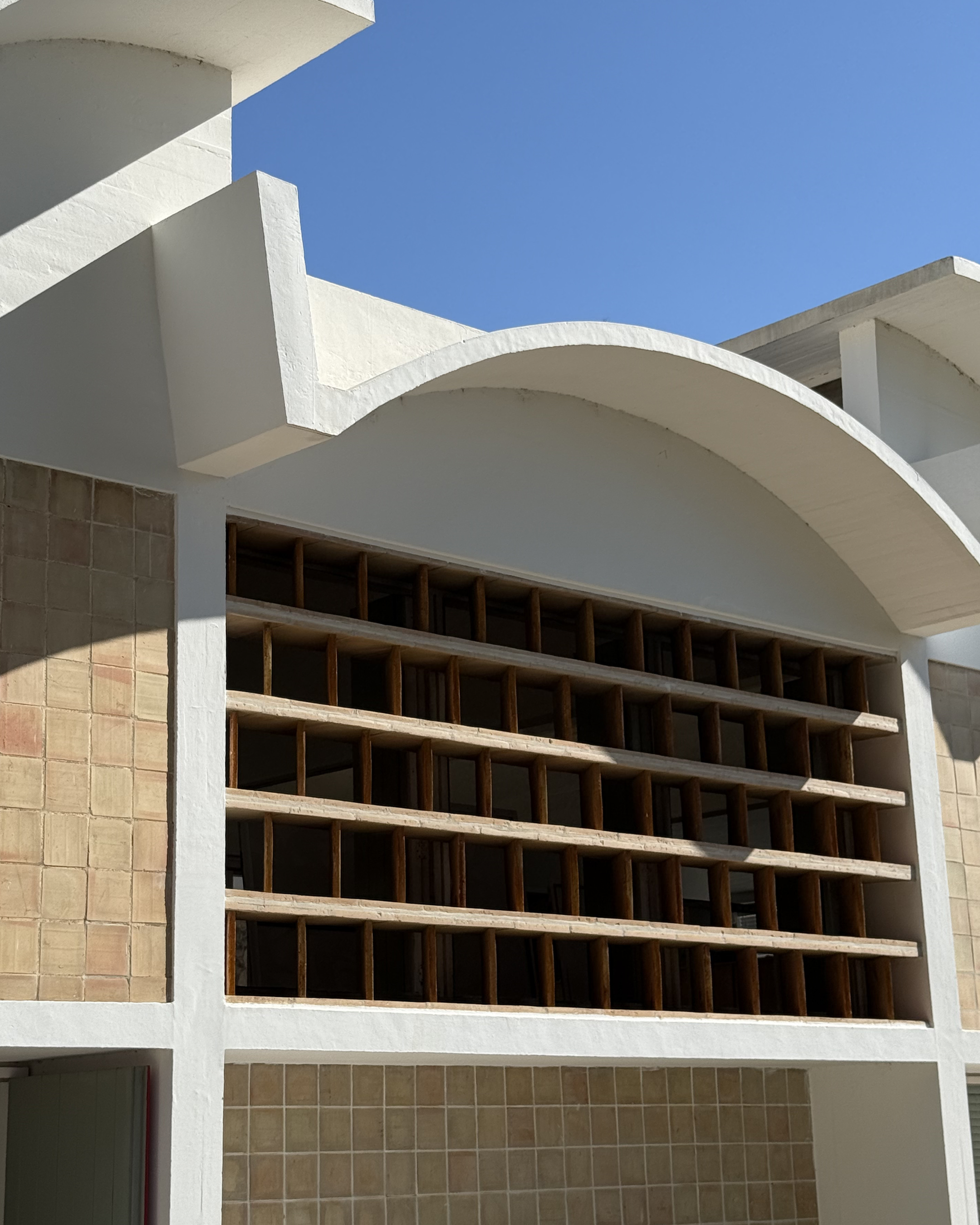 Curved white architecture and wooden sun screens at the Fundació Miró Mallorca, set against a clear blue Mediterranean sky.