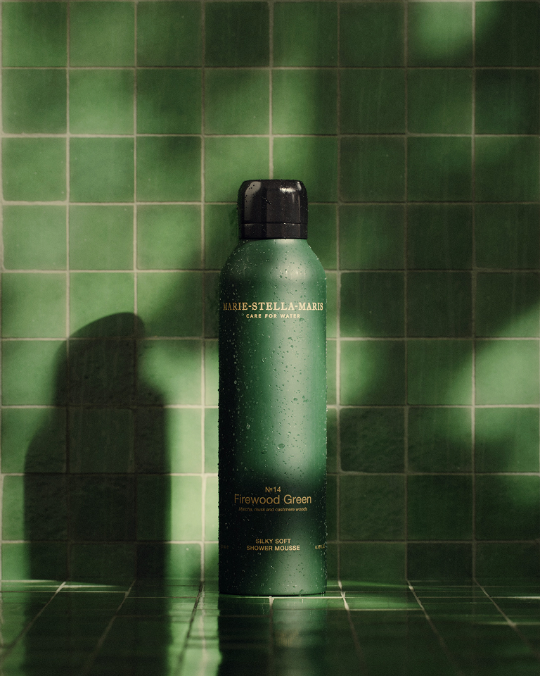 Marie-Stella-Maris No. 14 Firewood Green shower mousse covered in water droplets, displayed against glossy green bathroom tiles.