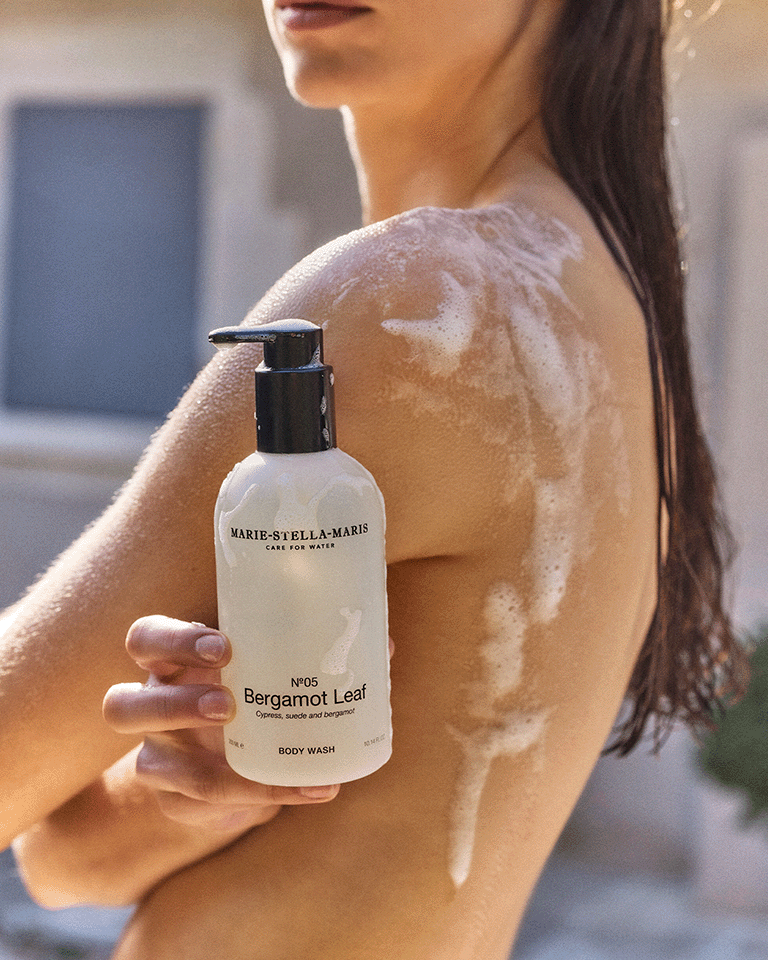 Person applying Marie-Stella-Maris No.05 Bergamot Leaf limited edition summer scent body wash 300 ml, with foam on the shoulder, highlighting the product in a warm, sunlit setting.