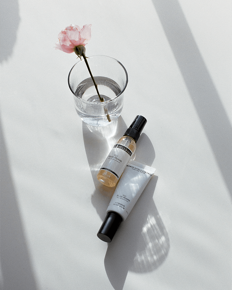 Marie-Stella-Maris No.10 Rock Roses limited edition Mother’s Day gift set essentials, featuring an intensive hand balm and room spray, styled with a delicate pink rose in a glass on a sunlit surface.