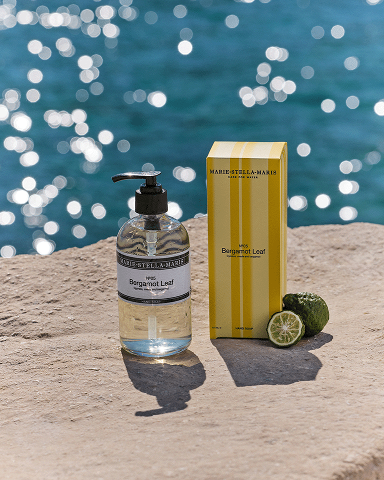 Marie-Stella-Maris No.05 Bergamot Leaf limited edition summer scent hand soap 250 ml with matching yellow-striped packaging, displayed on a sunlit stone surface by the sea with fresh bergamot and sparkling water in the background.