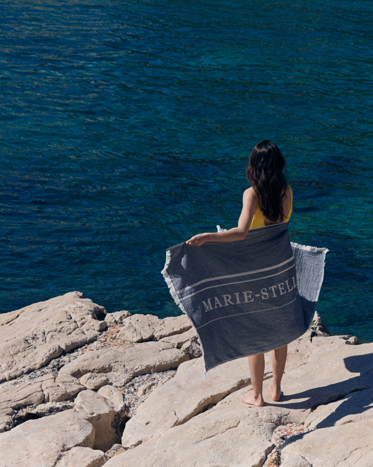 Hero banner for the Marie-Stella-Maris summer campaign, featuring a person standing on a rocky shoreline holding a towel and overlooking the sea, highlighting the new limited edition No.05 Bergamot Leaf scent.