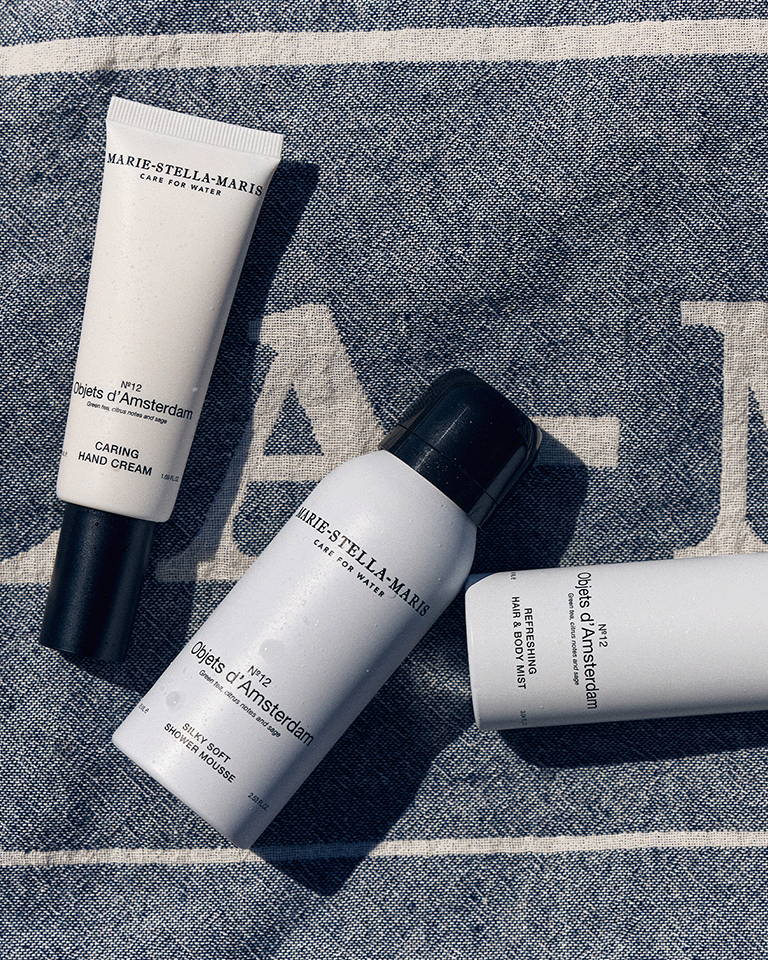 Marie-Stella-Maris No.12 Objets d’Amsterdam summer body care essentials, featuring caring hand cream, 75 ml travel-size Silky Soft Shower Mousse, and refreshing hair & body mist, styled on a Marie-Stella-Maris towel in a sunlit setting.