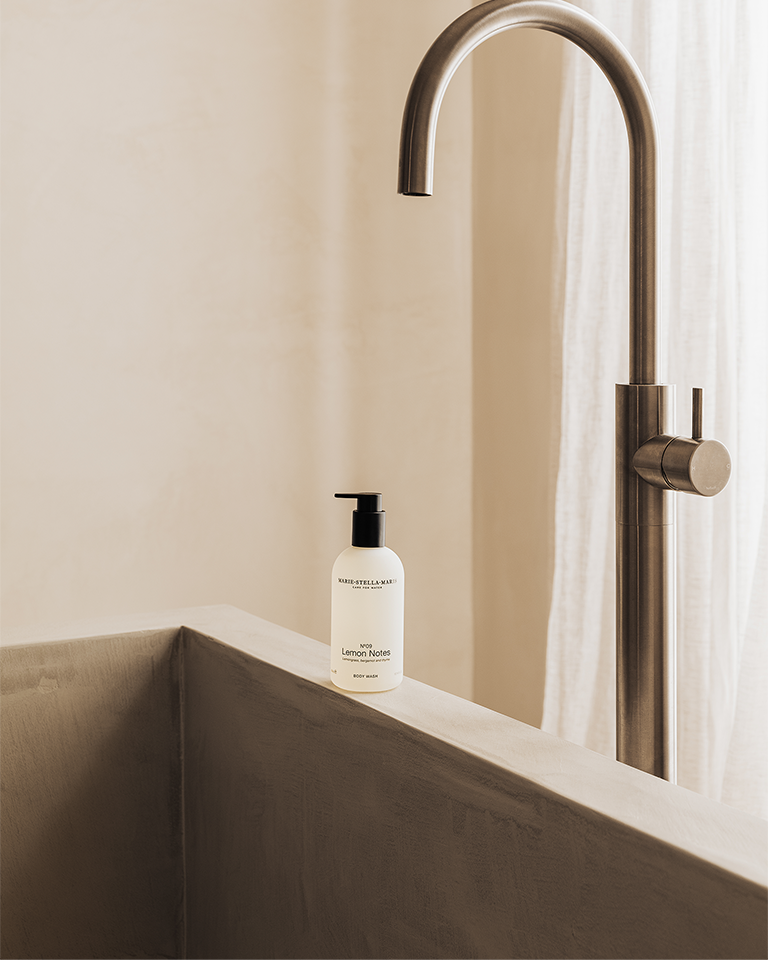 Bottle of Body Wash Lemon Notes 300 ml with pump dispenser placed on edge of a beige bathroom sink below a modern faucet