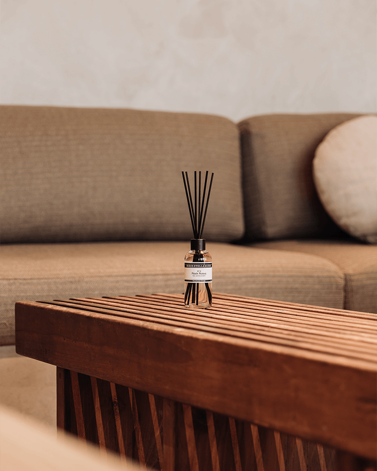 Marie-Stella-Maris Fragrance Sticks No.10 Rock Roses 100 ml placed on a wooden slatted coffee table in front of a soft beige sofa, with warm tones and a calm, minimalist living room setting.